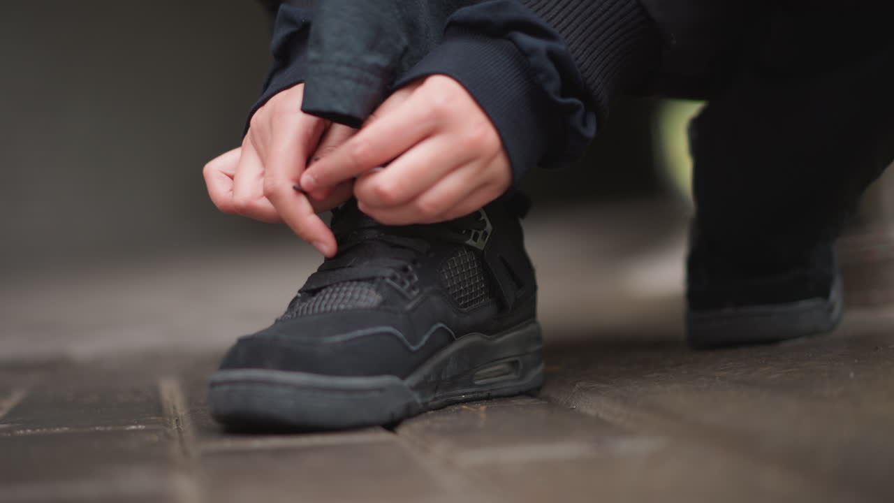 Studentessa che allaccia le scarpe da ginnastica all'aperto. Scena di un cortile umido che ritrae una studentessa che allaccia i lacci delle scarpe con disinvoltura. Primo piano di una studentessa che allaccia i lacci delle sue scarpe da ginnastica in un cortile universitario piovoso.