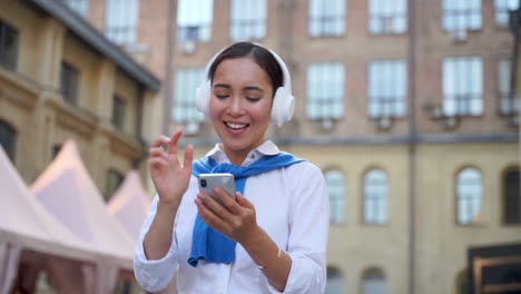 cheerful woman listening to music with headphones and walking down the street