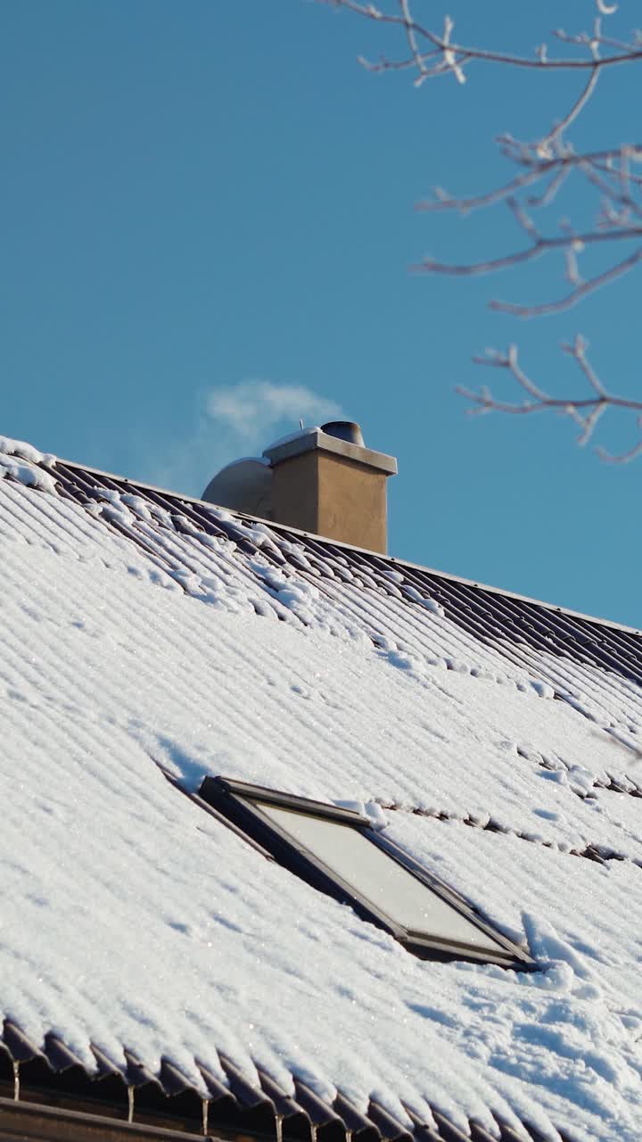 Vertical video of white smoke coming out of a chimney in winter. Roof covered with snow. Keeping home warm.