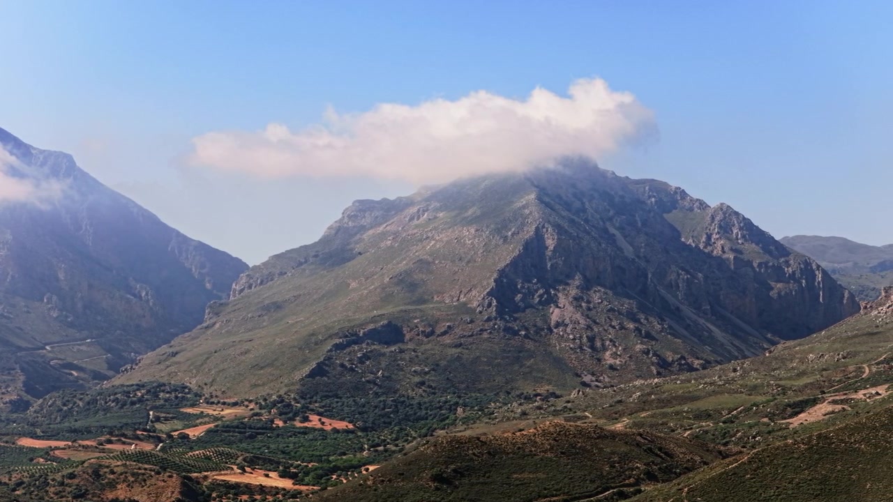 Vista aerea con drone di una cima montuosa rocciosa avvolta dalle nuvole sopra una valle verde, Creta, Grecia