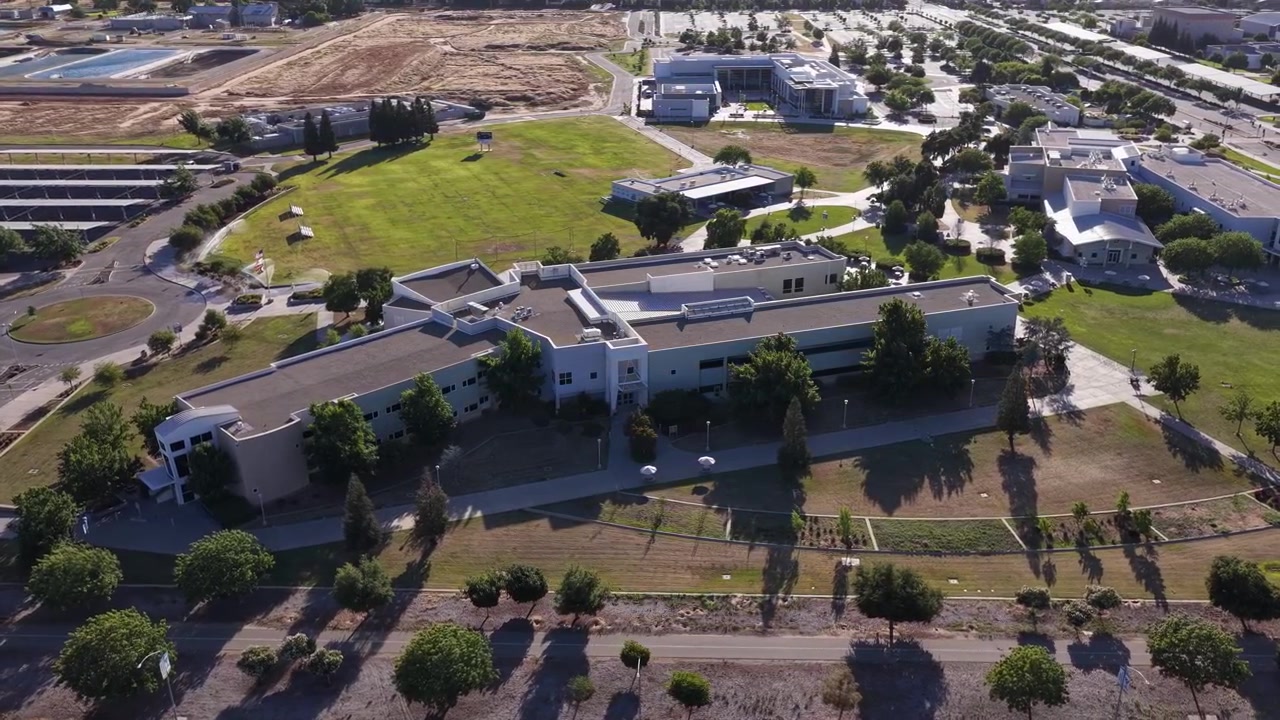 Drone perspective slowly orbiting the modern campus buildings and green lawns of Clovis Community College in Fresno, California, showcasing the academic and educational environment