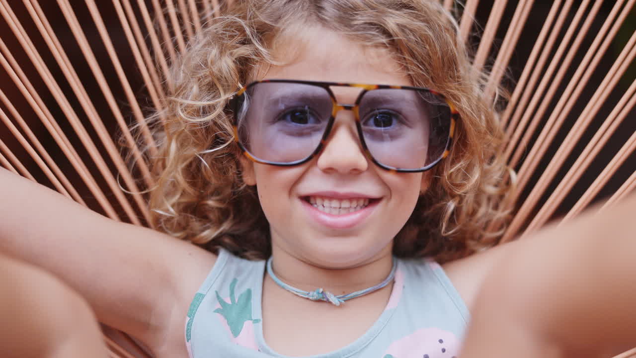 Cool little girl in a garden chair with sunglasses making faces