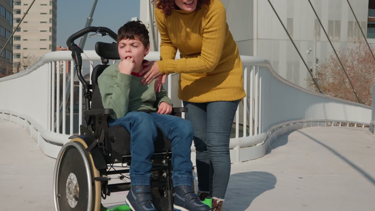 Child in wheelchair with caregiver outdoors on bridge