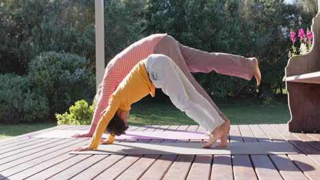 senior biracial grandmother and grandson doing yoga, stretching on terrace, slow motion