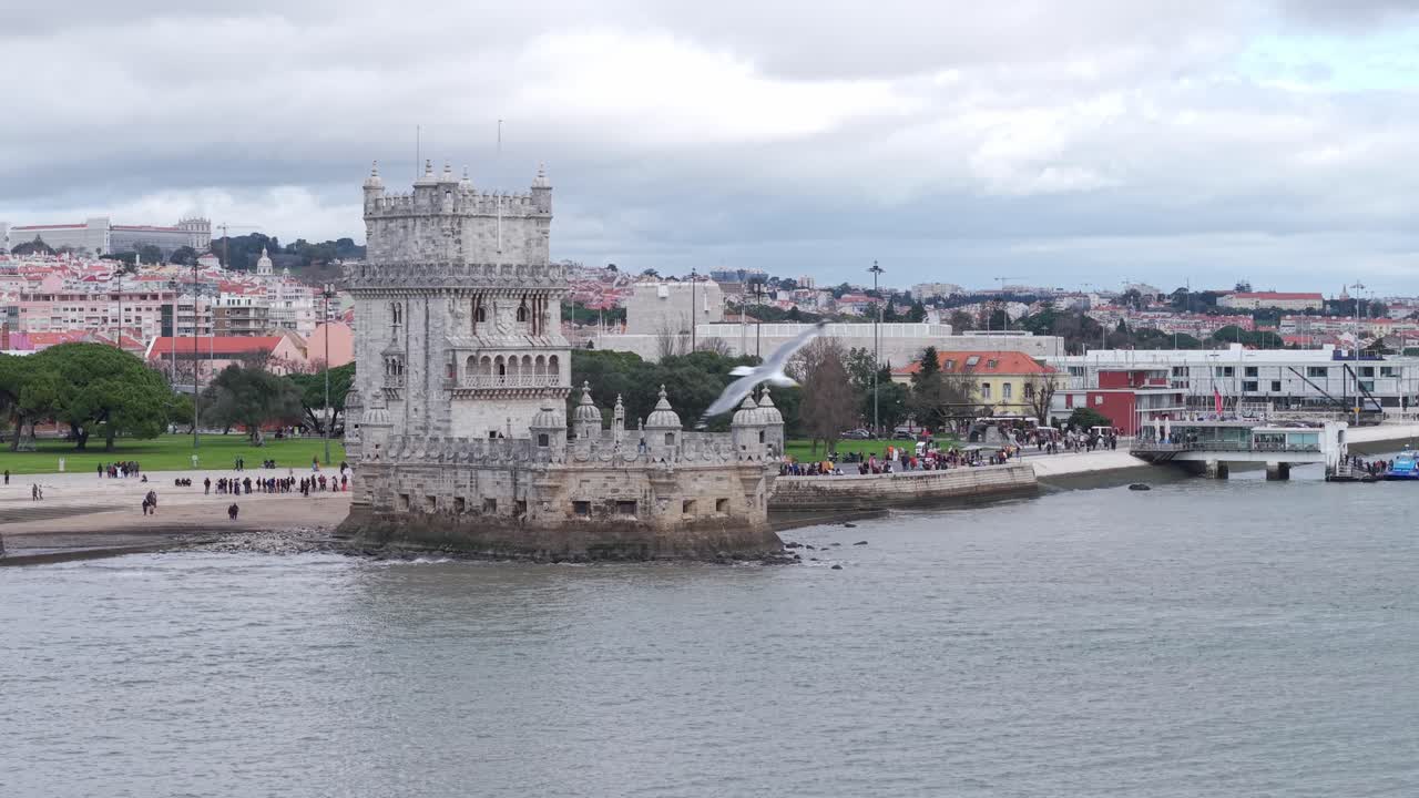 Belémská věž na břehu řeky Tejo s davy turistů, Lisabon, letecký oddalující se záběr.