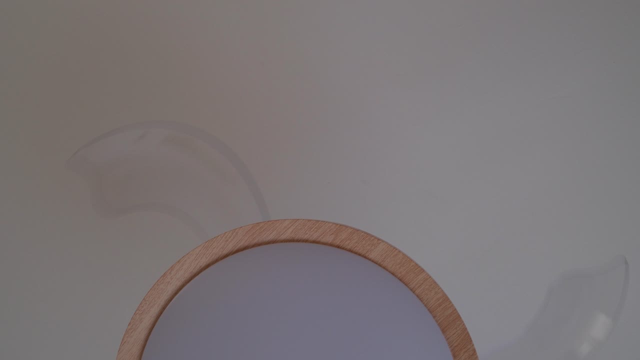 Un moderno ventilatore in legno gira dolcemente su uno sfondo neutro per un'estetica minimalista.