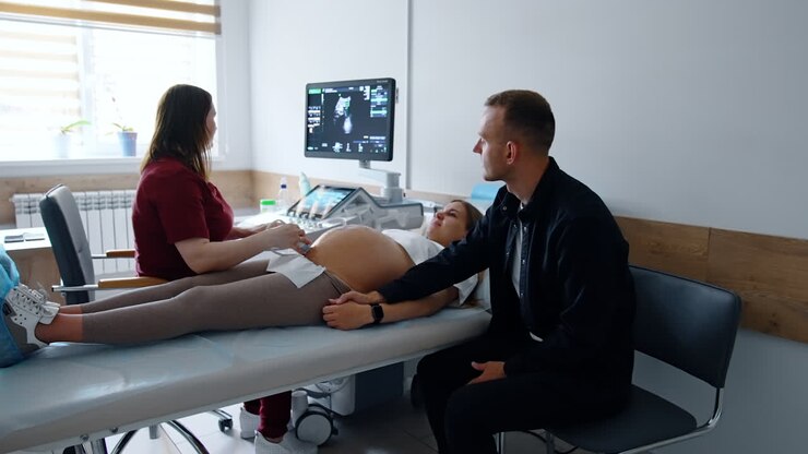 Female doctor checks the woman on last stages of pregnancy on ultrasound machine. Supporting man looks at the screen.