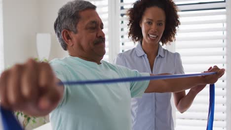Mixed-race-female-physiotherapist-helping-senior-man-exercise-using-exercise-band