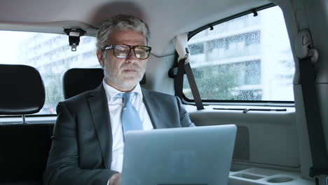 focused senior businessman using laptop in car