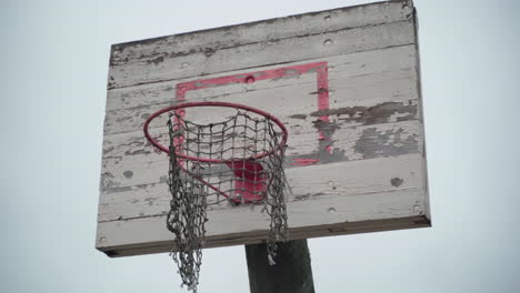 old basketball hoop with torn net hanging in wind and peeled off paint