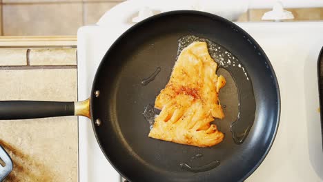 placing a seasoned salmon fillet in a frying pan with hot oil for a tasty meal - overhead view