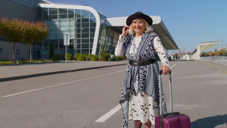 Portrait-of-senior-retired-woman-tourist-near-airport-terminal-waiting-boarding-on-plane,-traveling