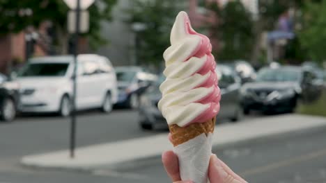mano sosteniendo un cono de helado suave y colorido en primer plano y girándolo sobre sí mismo en un agradable y ajetreado día de verano