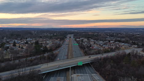 aerial view of multi-lane highway interchange at dusk with traffic flowing and residential area in background. timelapse