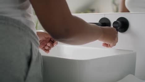 close up of african-american person washing hands in the sink and using white towel.