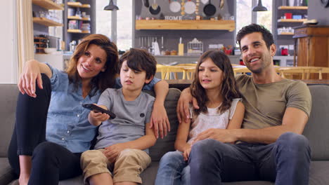 Family-Sitting-On-Sofa-In-Open-Plan-Lounge-Watching-Television