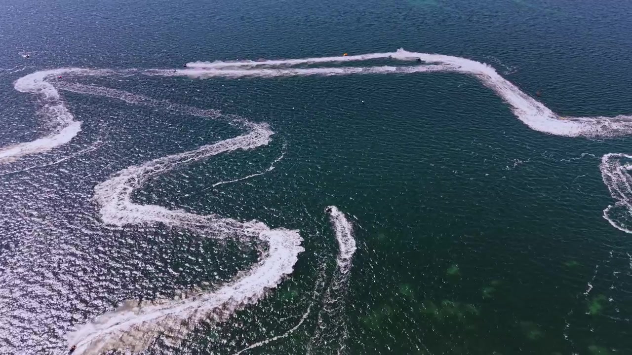 Waves create trails from jet skis on clear water near the coastline
