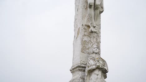 a close-up view of a stone crucifix depicting jesus, highlighting details of the sculpture against a plain sky