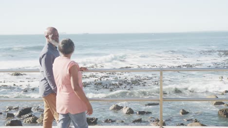 happy senior african american couple embracing on promenade by the sea, slow motion