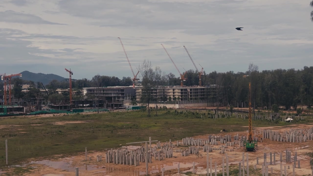 Medium close up of an active high rise construction site featuring cranes, concrete foundation poles and unfinished building structures in an urban development area.