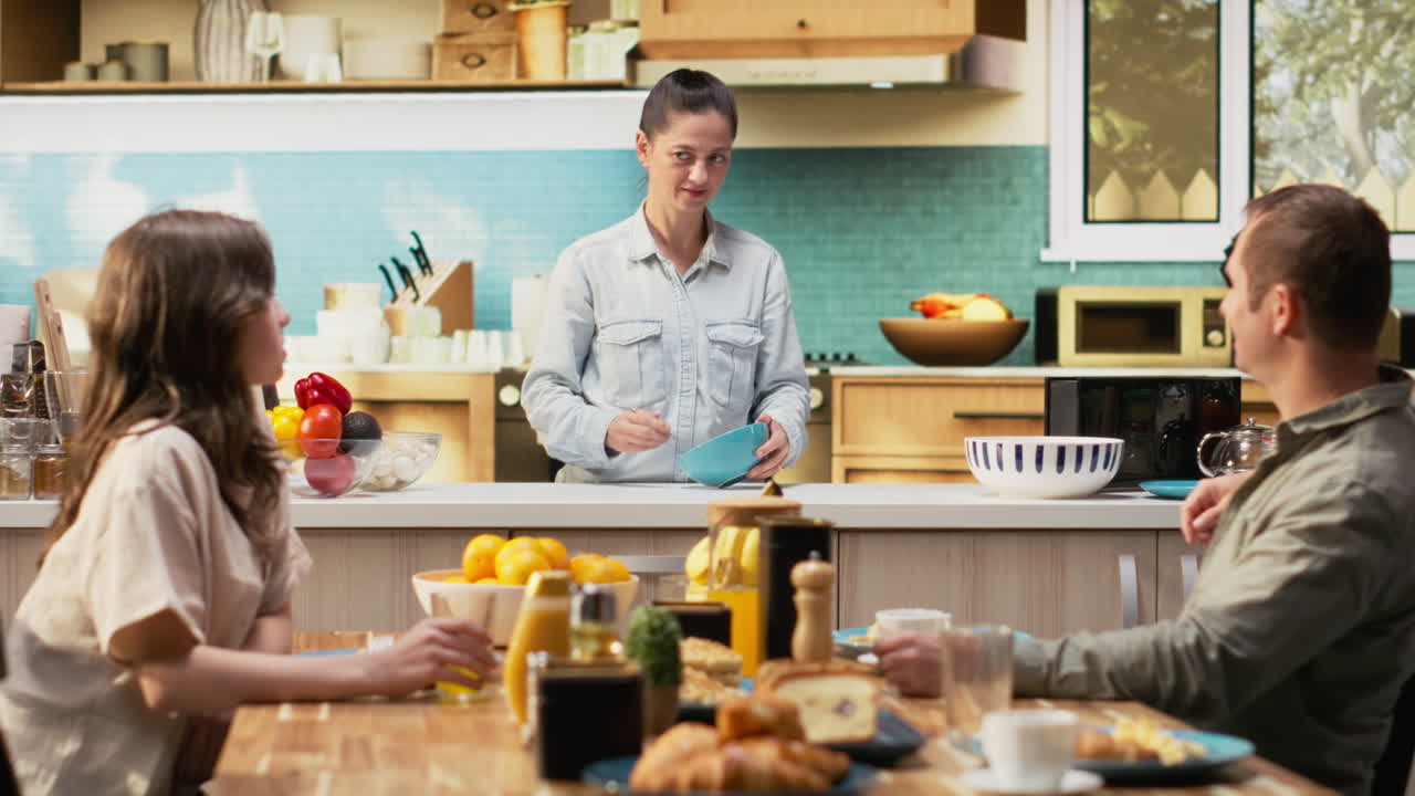 Mother preparing breakfast in the morning light while family waits at the table