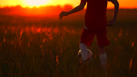 primer plano de un jugador de fútbol de pie corriendo al atardecer con una pelota en el campo la cámara se mueve detrás del niño.