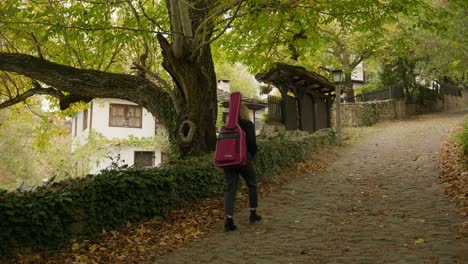 el músico camina por el camino empedrado de otoño de un pueblo rústico encantado.