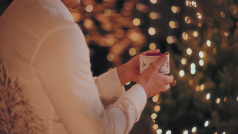 hombre sosteniendo una taza de café mientras está sentado en una casa iluminada durante la navidad