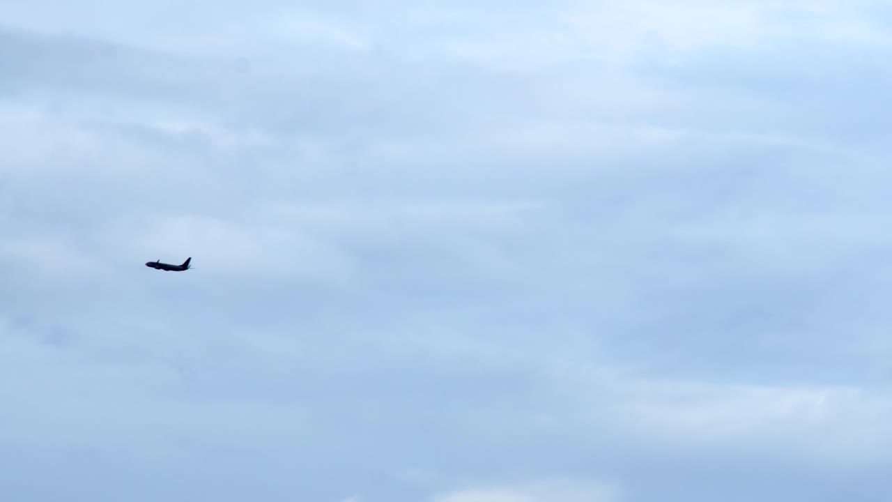 Fly flyver i det fjerne mod en overskyet, stemningsfuld himmel - totalbillede silhuet