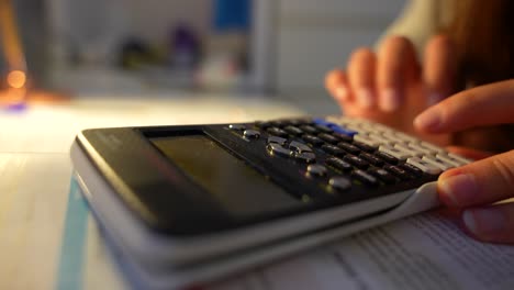 primer plano de los dedos de los estudiantes usando una calculadora científica por la noche