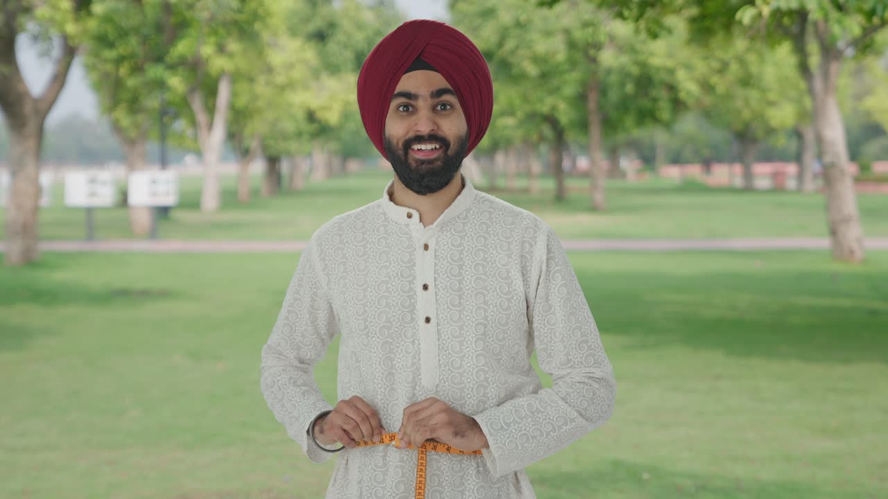 hombre indio sikh feliz midiendo la cintura usando cinta de pulgada en el parque