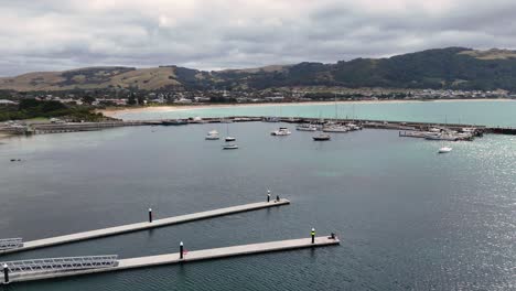 Drone footage captures Apollo Bay's scenic harbor with boats, pier, and surrounding landscape under cloudy skies