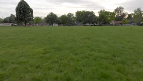 Fly-fast-and-close-over-park-grass-with-people-play-soccer-in-the-background