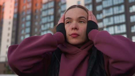 close up of determined young woman pushing hair back from face with hand on urban sports court background, buildings out of focus, natural motion wrist braces visible, capturing candid athletic scene