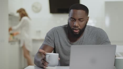 concentrated black man working laptop computer at open kitchen.