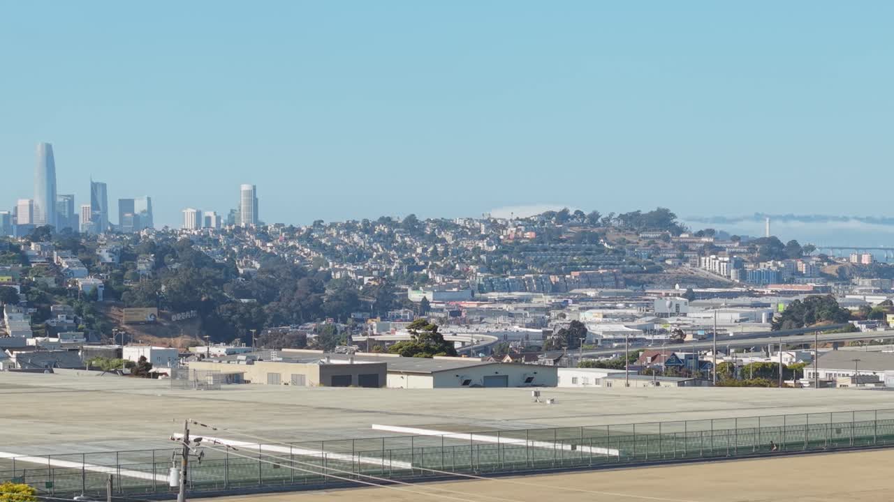 Golden sunlight brushes across Bernal Heights as rows of houses stretch down toward the city basin. Downtown San Francisco is seen in the distance.