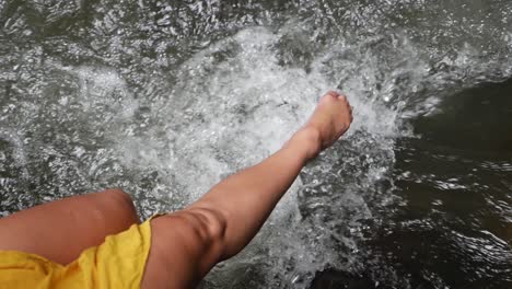 Una-Toma-De-Primer-Plano-En-Cámara-Súper-Lenta-De-Una-Mujer-Joven-Salpicando-Sus-Piernas-En-El-Río-Mientras-Se-Sienta-En-Una-Roca-En-La-Jungla-De-Bali