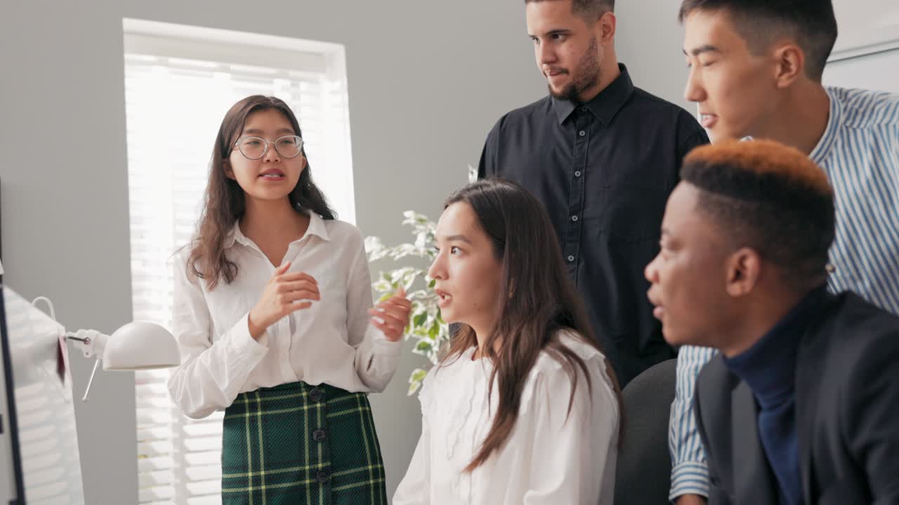 mujer de negocios, mujer elegante con gafas se encuentra en el escritorio de los compañeros de trabajo mirando el monitor de la computadora, discuten el proyecto, la campaña, la tormenta de ideas, el líder motiva al equipo a trabajar