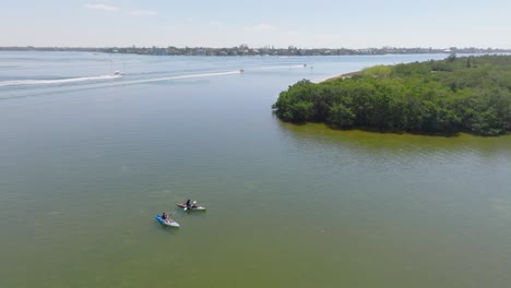 Kayakistas-En-Una-Bahía-De-Florida-Cerca-De-Los-Túneles-De-Manglares-De-Lido-Key-Con-Barcos-Que-Pasan-Al-Fondo