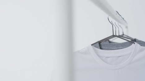 video of white and grey t shirts on hangers and copy space on white background