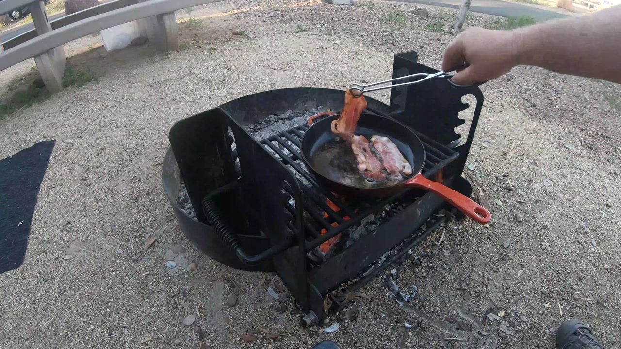 焚き火の上で鋳鉄製スキレットでベーコンを調理する