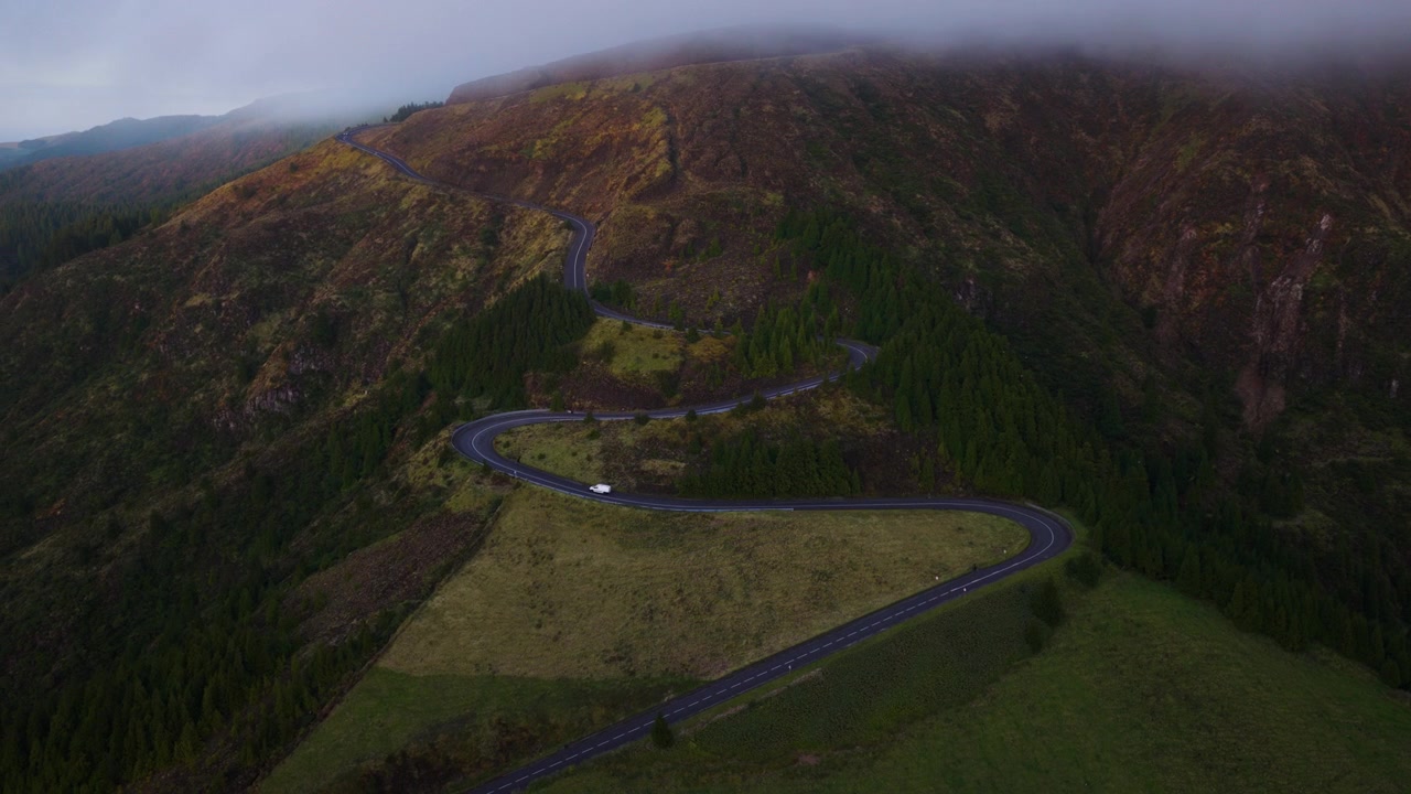 En slingrande bergsväg passerar genom höglandet på ön São Miguel på Azorerna, Portugal, vid solnedgången. Flygfoto.