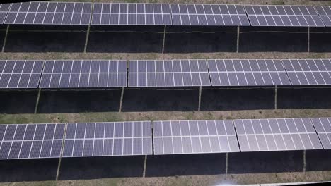 sun reflects off array of black solar panels in low aerial flyover