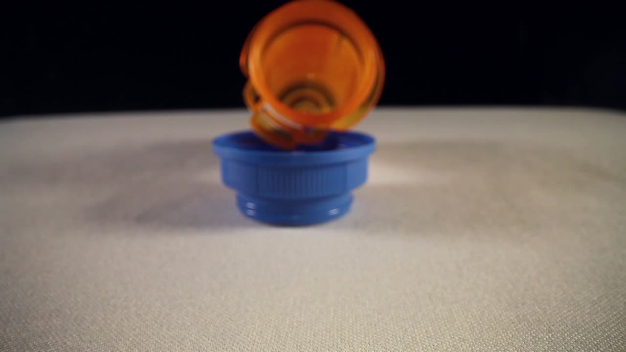 moviéndose más allá de la tapa azul vacía de la botella, empujando lentamente en toda la longitud de una botella naranja de píldoras recetadas