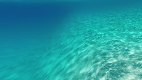 underwater view: steep sandy slope, sun reflects off turquoise bottom