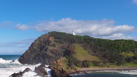 a serene 15-second video of byron bay's lighthouse, capturing waves crashing against the rocky coastline under a clear blue sky