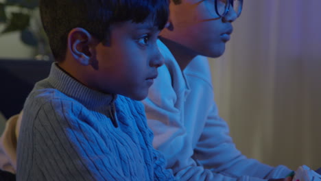 Close-Up-Of-Two-Young-Boys-At-Home-Playing-With-Computer-Games-Console-On-TV-Holding-Controllers-Late-At-Night-1