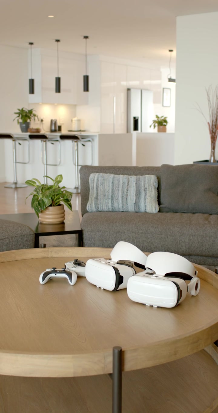 Vertical video: Camera is panning to three VR headsets and white gamepad on table, centering view