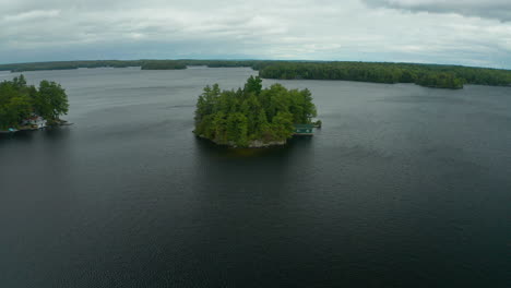 aerial view flying over a small isolated island with a cottage on it in the middle of a lake