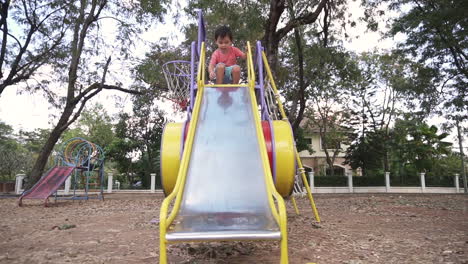 east asian boy kid having fun playing at a park with toy cars and going down the slider after school